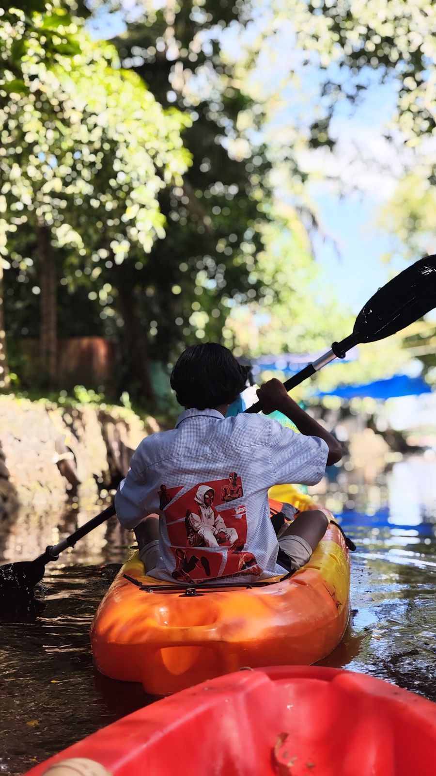 A paddler in an orange kayak on a narrow canal
